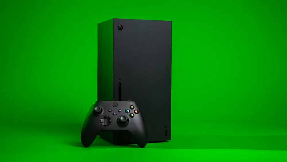 A black Xbox Series X console standing upright with a matching controller in front of it, against a bright green background.